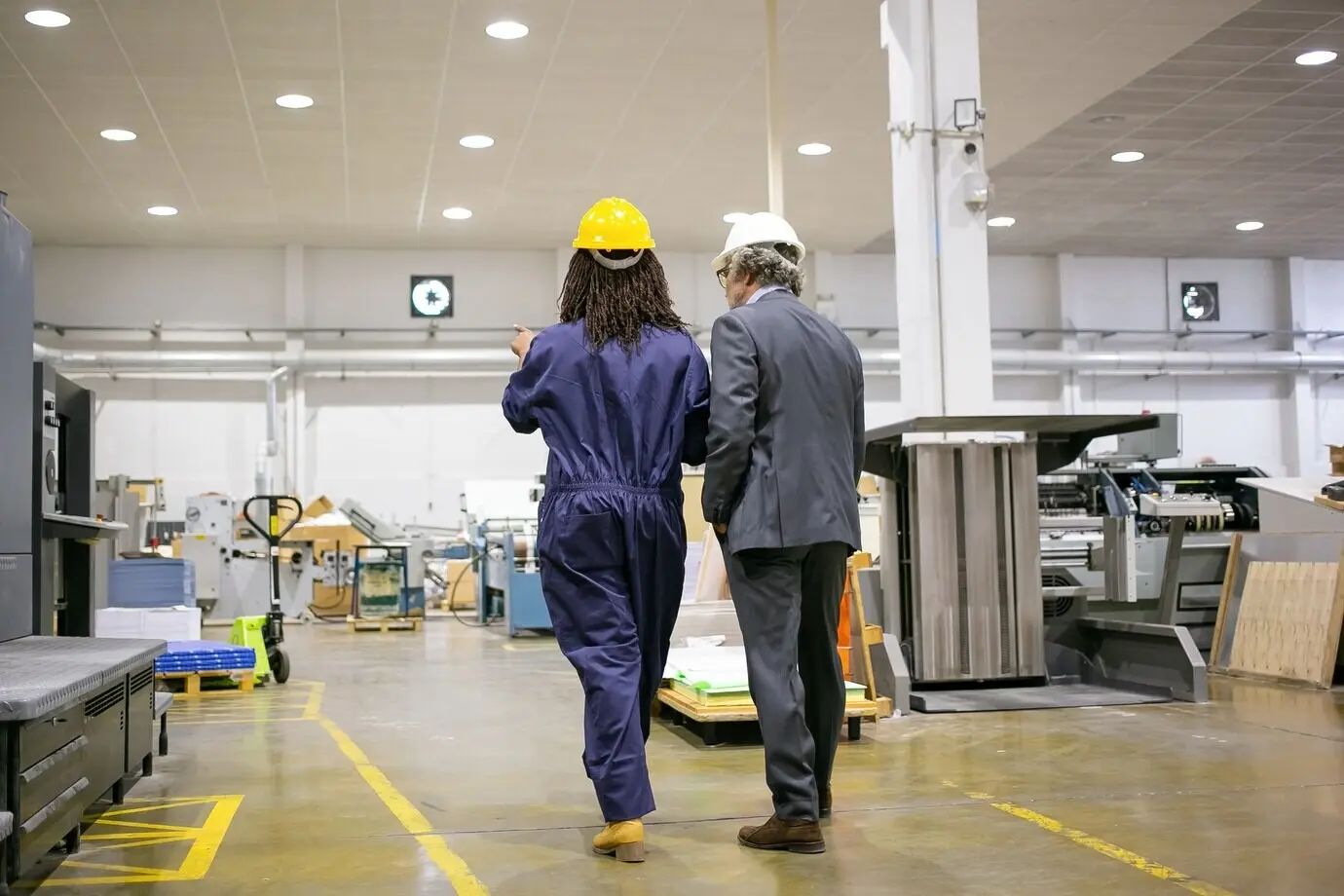 Rückansicht eines Chefs, der in der Fabrik steht und einem Fabrikarbeiter zuhört.